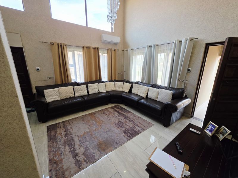Spacious living room featuring double-volume ceilings, large windows for natural light, polished porcelain floor tiles, and a wall-mounted air conditioning unit.