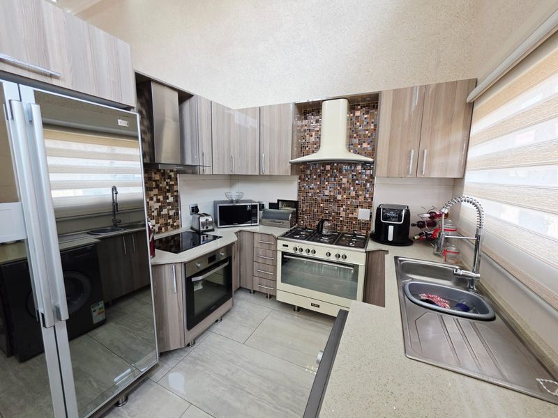 A well-appointed kitchen featuring modern wood-grain cabinetry, stone countertops, a mosaic tile backsplash, and high-quality built-in cooking appliances.