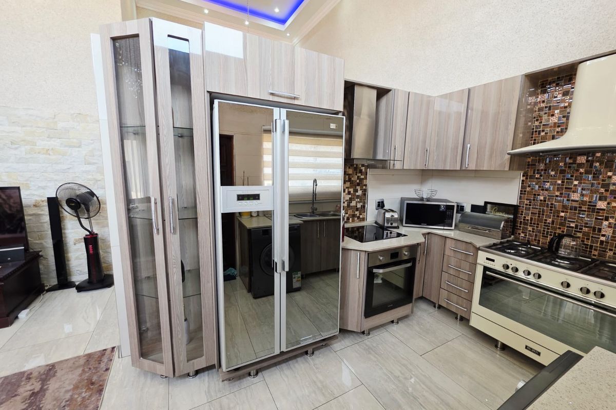 Modern kitchen featuring wood-grain cabinetry, mosaic tile backsplash, integrated appliances, and high-end recessed ceiling lighting with decorative cove details.