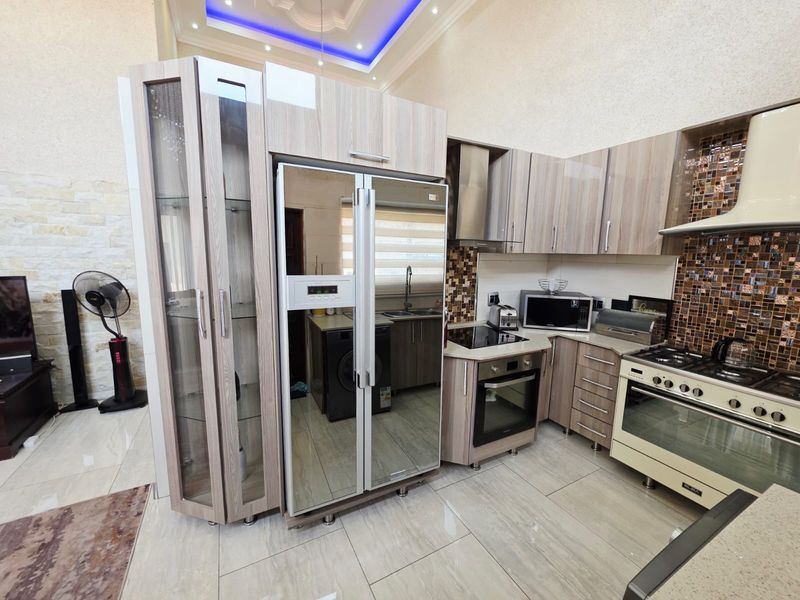 Modern kitchen featuring wood-grain cabinetry, mosaic tile backsplash, integrated appliances, and high-end recessed ceiling lighting with decorative cove details.