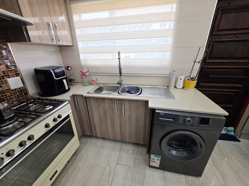 A well-maintained kitchen featuring stone countertops, laminate cabinetry, a gas stove with oven, and a double bowl sink with a modern mixer tap.