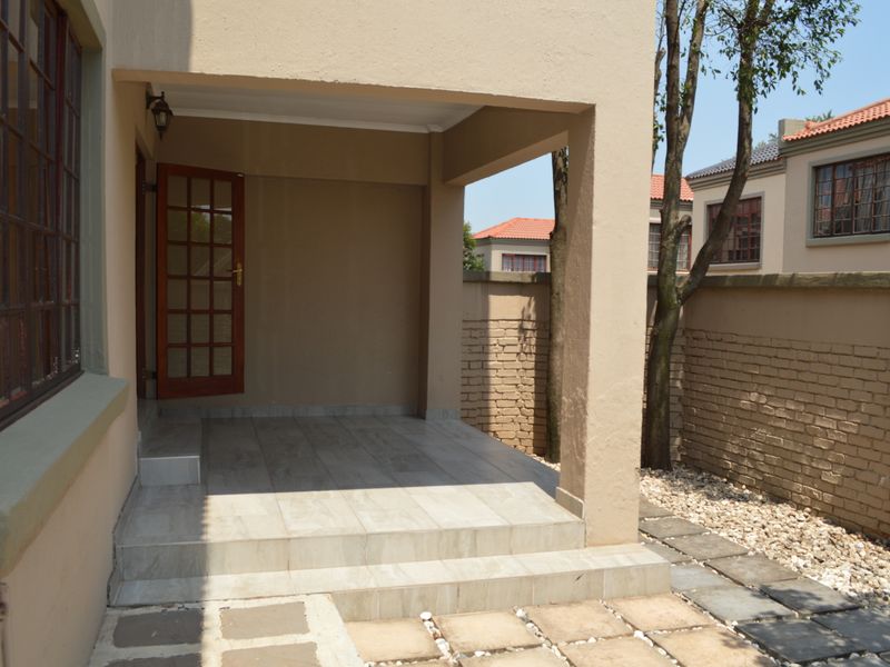A covered patio area featuring tiled flooring and a timber-framed glass door, providing a clean outdoor space for relaxation.