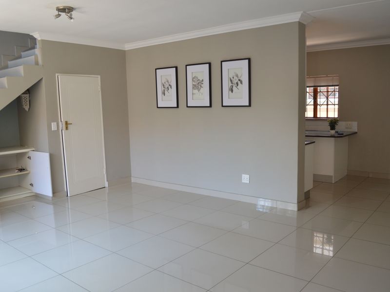 Spacious open-plan living area featuring neutral tiled flooring, a staircase with built-in storage, and a partial view into the kitchen area.