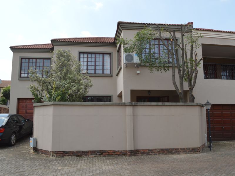 Front elevation of a double-storey townhouse featuring a paved driveway, timber garage doors, and a balcony with a tiled roof.