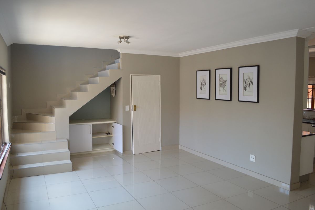 Spacious living area featuring neutral tiled flooring, a staircase with integrated under-stair storage, and clean, well-maintained wall finishes.
