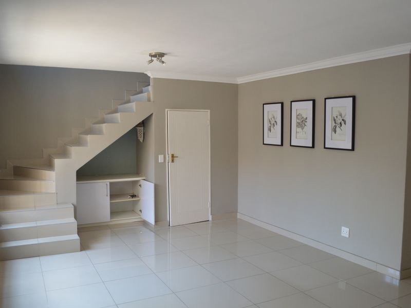Spacious living area featuring neutral tiled flooring, a staircase with integrated under-stair storage, and clean, well-maintained wall finishes.