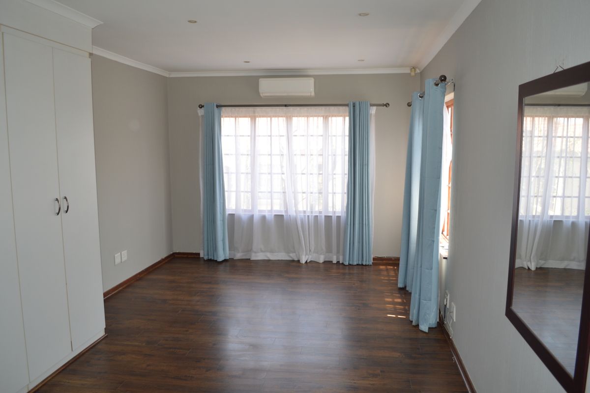 A spacious, empty bedroom featuring laminate flooring, built-in wardrobes, and a wall-mounted air conditioning unit, offering a clean and neutral living space.