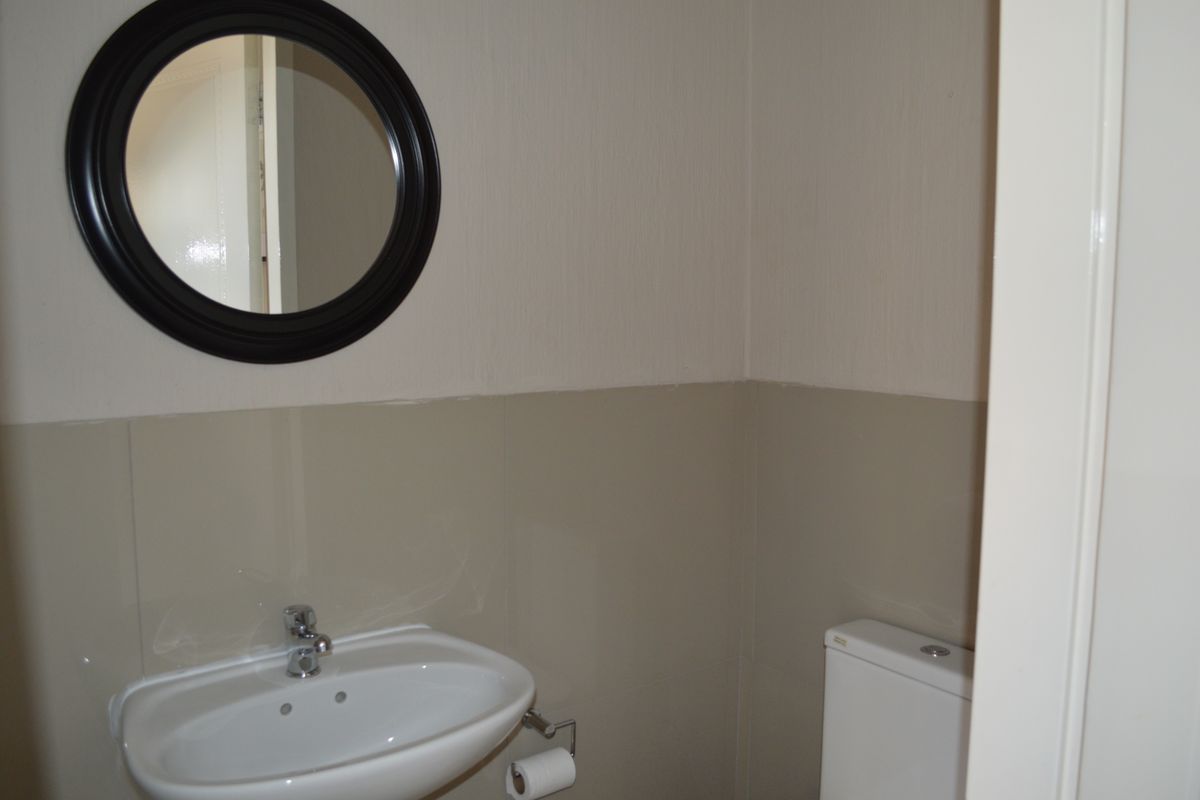 A compact guest bathroom featuring a wall-mounted basin with chrome mixer tap and a standard toilet with neutral tiled splashback.