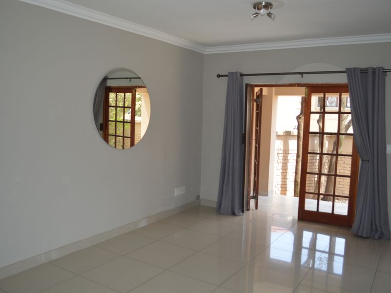 A bright, empty living room featuring neutral tiled flooring, ceiling cornicing, and wooden french doors providing access to an outdoor patio area.