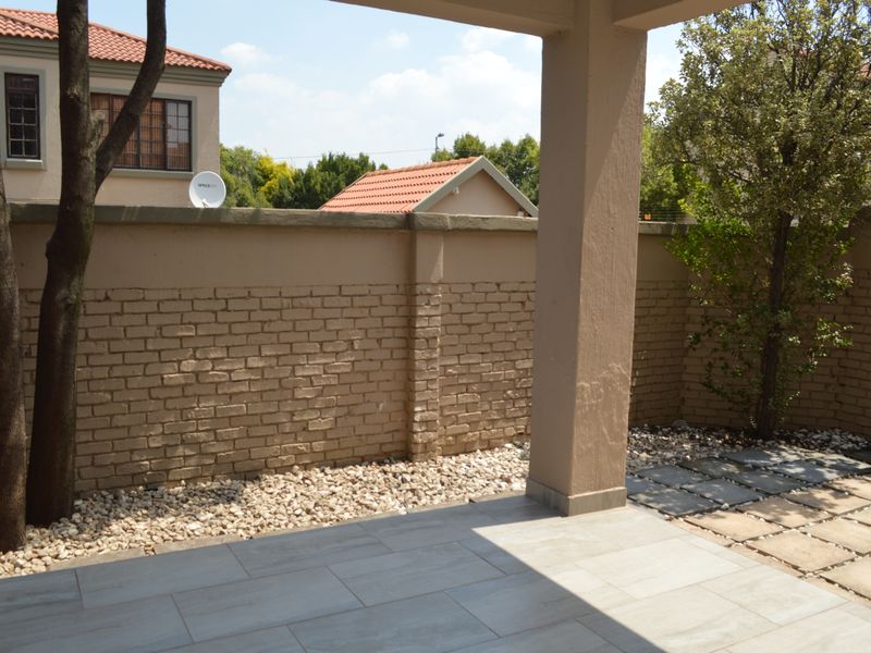 A covered patio area featuring tiled flooring and a brick boundary wall, offering a private outdoor space for relaxation.