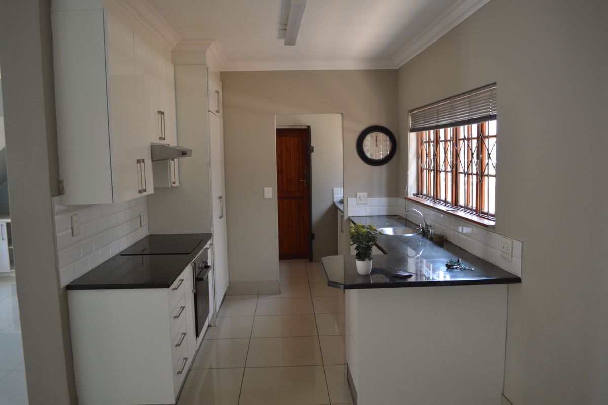 A functional kitchen featuring white cabinetry, granite countertops, a subway tile backsplash, and tiled flooring, with a window fitted with security bars.