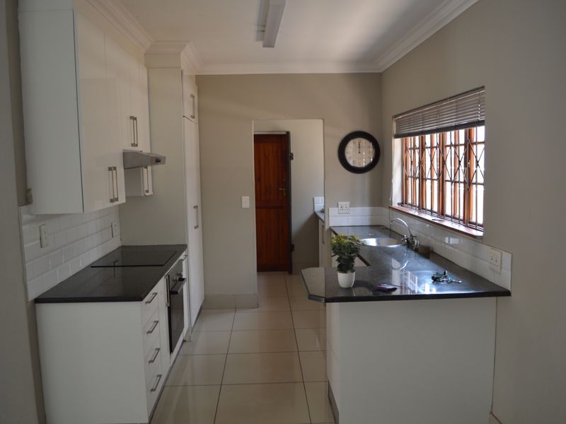 A functional kitchen featuring white cabinetry, granite countertops, a subway tile backsplash, and tiled flooring, with a window fitted with security bars.