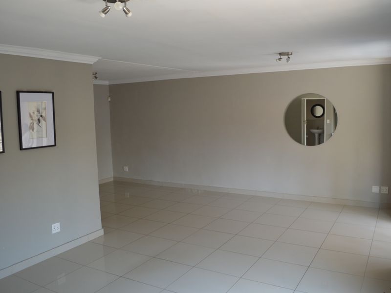A spacious, neutral-toned living area featuring polished tile flooring, modern spotlight lighting, and clean finishes, offering a versatile blank canvas for interior design.