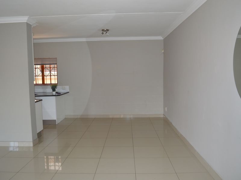 An open-plan living area featuring neutral tiled flooring, coved cornicing, and a partial view into the kitchen space.