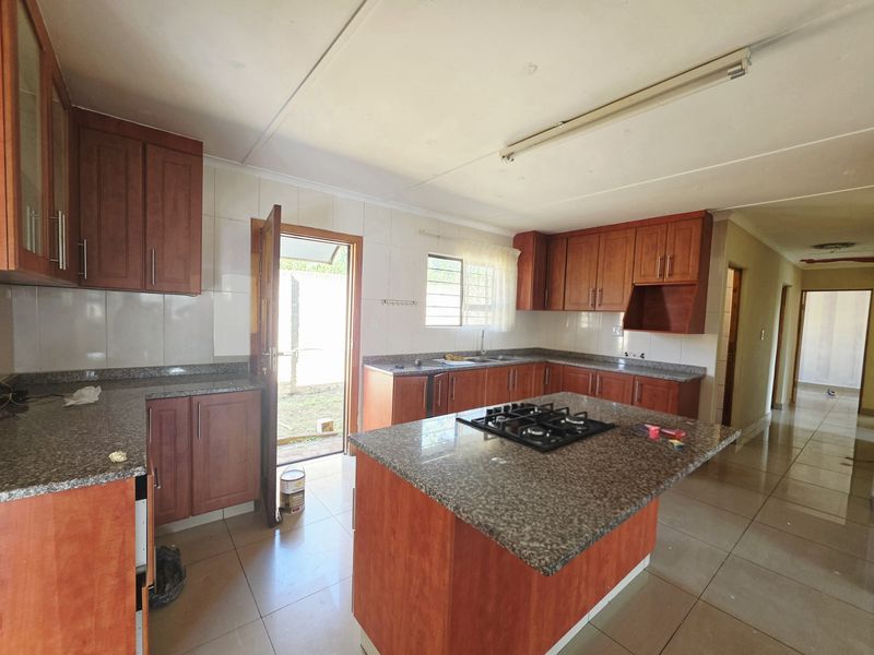 Spacious kitchen featuring granite countertops, wooden cabinetry, a central island with a gas hob, and direct access to the rear exterior.