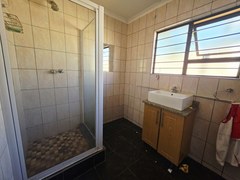 A functional bathroom featuring a shower enclosure, vanity cabinet with basin, and tiled finishes throughout, offering a clean space ready for potential modernization.
