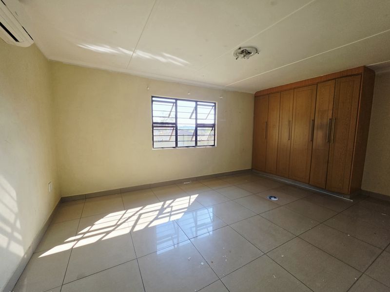 A vacant bedroom featuring tiled flooring, built-in wooden cupboards, and an installed air conditioning unit.
