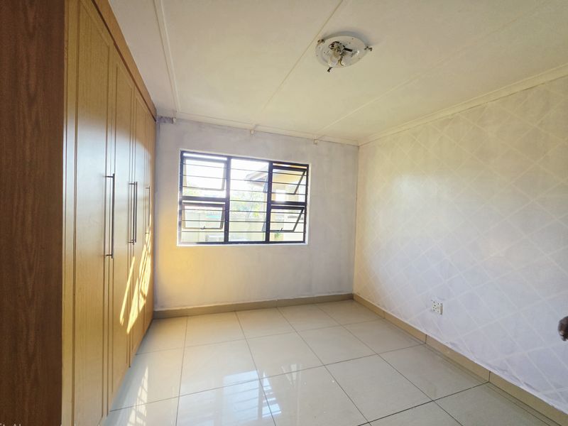 A vacant bedroom featuring built-in wooden cupboards, tiled flooring, and a window with security bars.