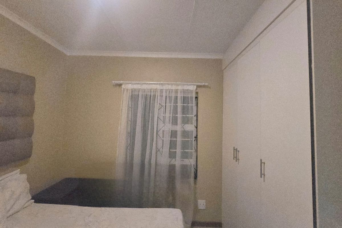A bedroom featuring built-in cupboards, security bars on the window, and neutral wall finishes.