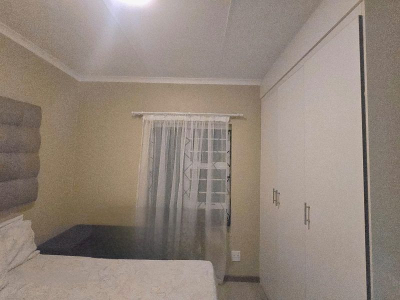 A bedroom featuring built-in cupboards, security bars on the window, and neutral wall finishes.