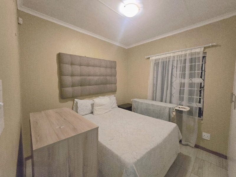 A functional bedroom featuring tiled flooring, security bars on the window, and neutral wall finishes.