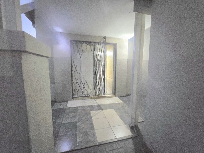 A covered outdoor patio area featuring tiled flooring and a security gate entrance, requiring maintenance and cosmetic updates.