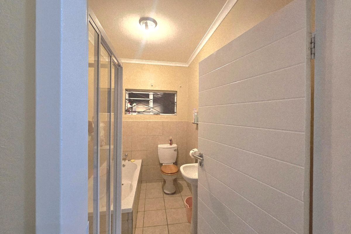 A functional bathroom featuring a shower enclosure, bathtub, pedestal sink, and toilet with neutral tiled flooring and wall finishes.