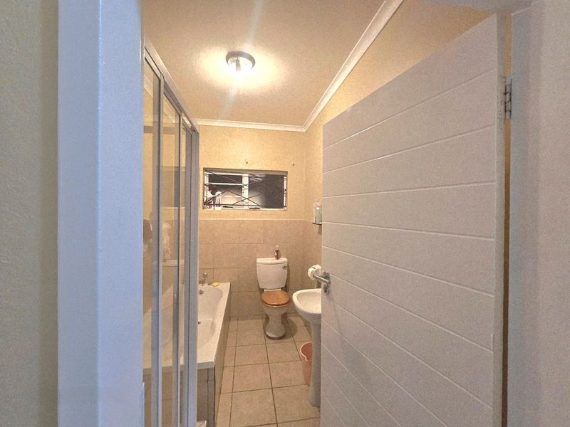 A functional bathroom featuring a shower enclosure, bathtub, pedestal sink, and toilet with neutral tiled flooring and wall finishes.