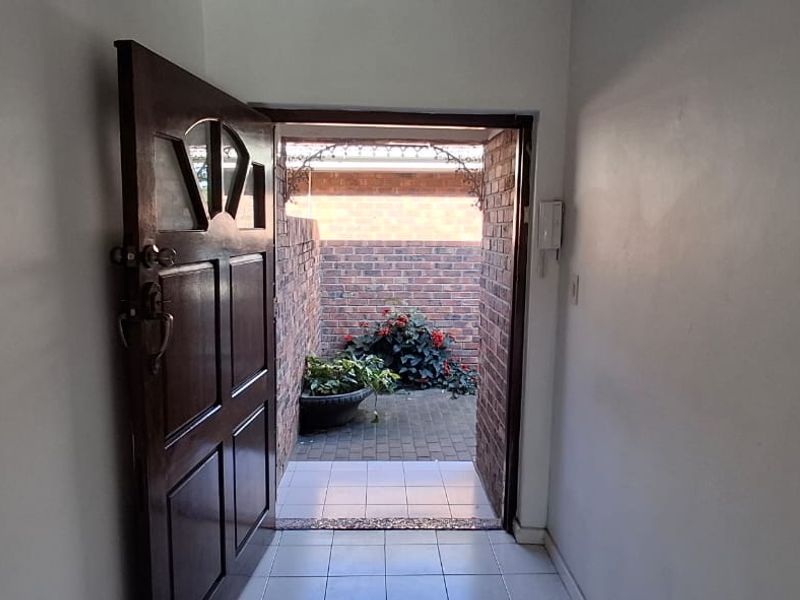 Entrance foyer featuring a timber front door, tiled flooring, and an intercom system, leading out to a private paved courtyard area.