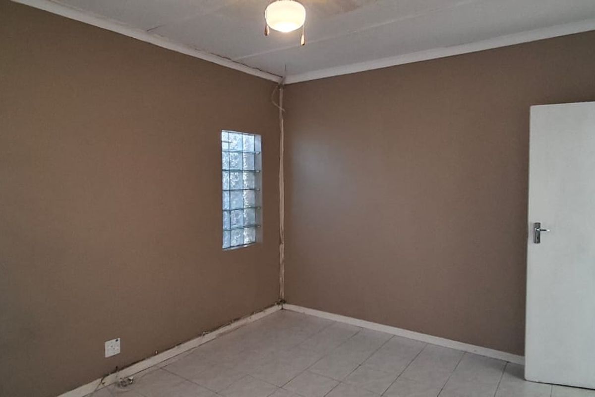 An empty bedroom featuring tiled flooring, a glass block window, and a ceiling fan, offering a blank canvas for renovation.
