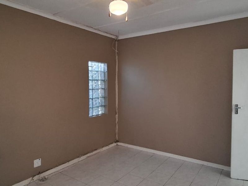 An empty bedroom featuring tiled flooring, a glass block window, and a ceiling fan, offering a blank canvas for renovation.