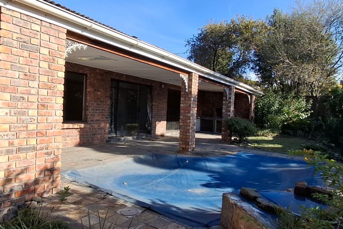 Rear exterior view featuring a covered patio with a built-in braai, overlooking a swimming pool with a pool cover and established garden.