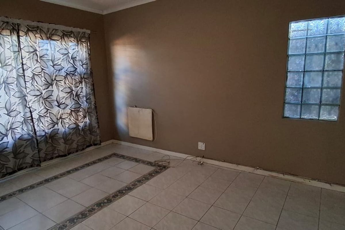 An empty living room featuring tiled flooring, a unique glass block window, and a wall-mounted heater, ready for renovation or staging.