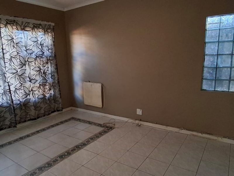 An empty living room featuring tiled flooring, a unique glass block window, and a wall-mounted heater, ready for renovation or staging.