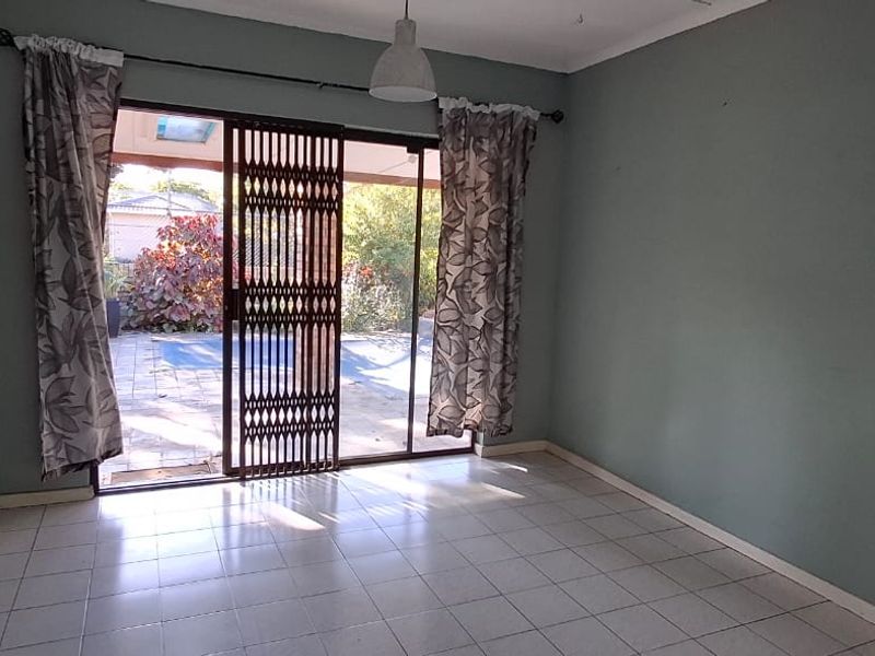 An empty living room featuring a painted brick wall, tiled flooring, and a sliding glass door with a security gate leading to the patio.