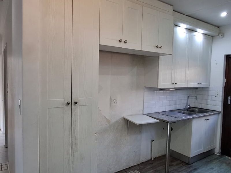 A compact kitchen featuring white cabinetry, a stainless steel sink, and subway tile backsplash, currently requiring wall repairs and cosmetic updates.