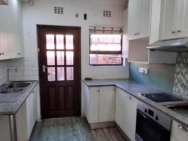 A functional kitchen featuring granite countertops, built-in cabinetry, integrated oven and hob, and a rear access door.