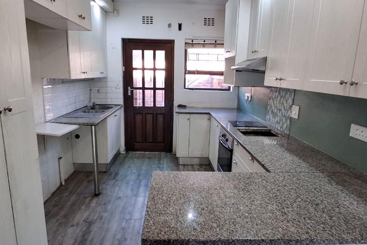 A functional kitchen featuring granite countertops, built-in cabinetry, an integrated oven and hob, and a tiled backsplash with direct access to the exterior.