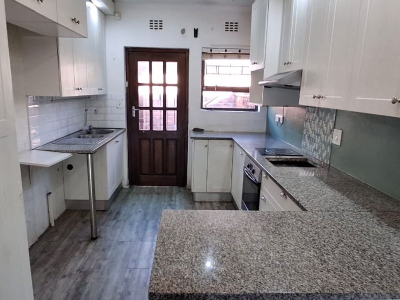 A functional kitchen featuring granite countertops, built-in cabinetry, an integrated oven and hob, and a tiled backsplash with direct access to the exterior.