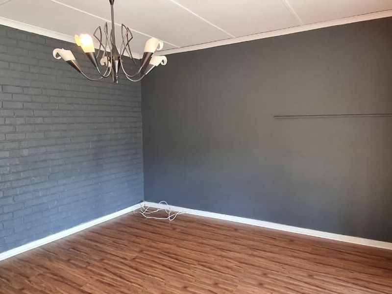 An empty living room featuring a dark grey exposed brick accent wall, laminate flooring, and a modern ceiling light fixture.