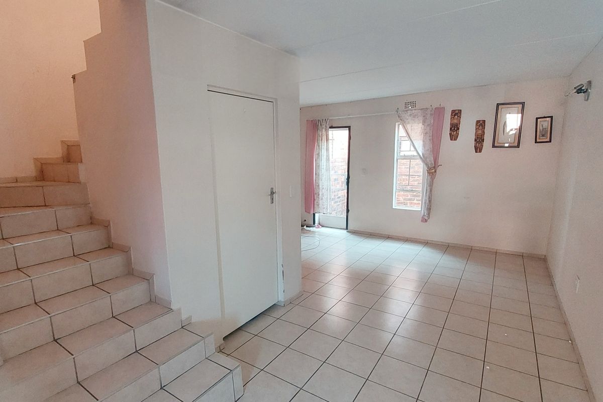An open-plan living area featuring ceramic floor tiles, a built-in staircase, and direct access to an outdoor space.