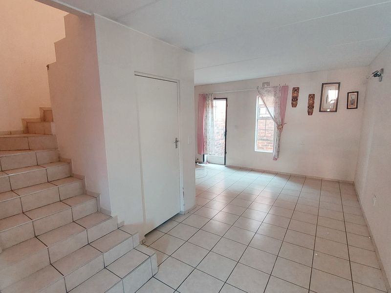 An open-plan living area featuring ceramic floor tiles, a built-in staircase, and direct access to an outdoor space.