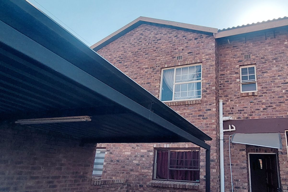 Rear view of the townhouse featuring a face brick facade, a covered carport area, and paved ground surface.