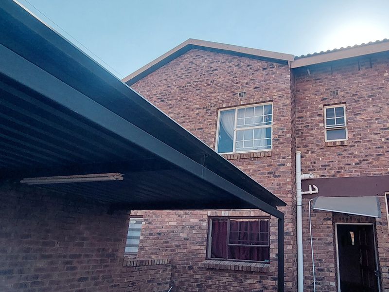 Rear view of the townhouse featuring a face brick facade, a covered carport area, and paved ground surface.