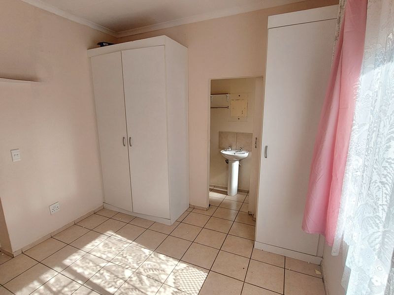 A bedroom featuring built-in cupboards and tiled flooring, with an adjoining small en-suite area containing a pedestal basin.
