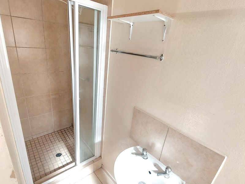 A functional bathroom featuring a shower enclosure with tiled walls, a pedestal basin with a tiled splashback, and a wall-mounted towel rail.