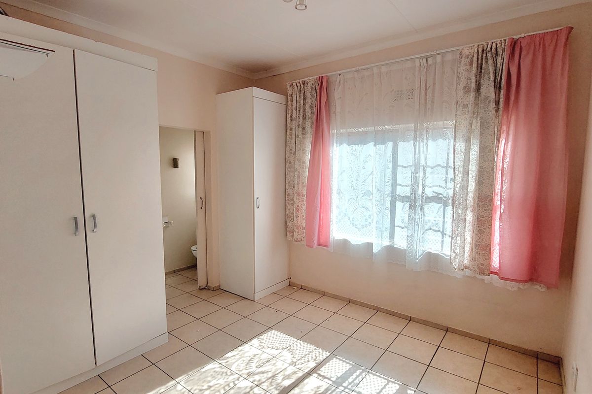 A bright, empty bedroom featuring tiled flooring and built-in cupboards, with an adjoining en-suite bathroom visible through the doorway.