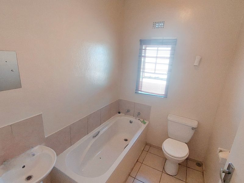 A functional bathroom featuring a pedestal basin, built-in bathtub, and toilet with neutral tiled flooring and splashbacks.