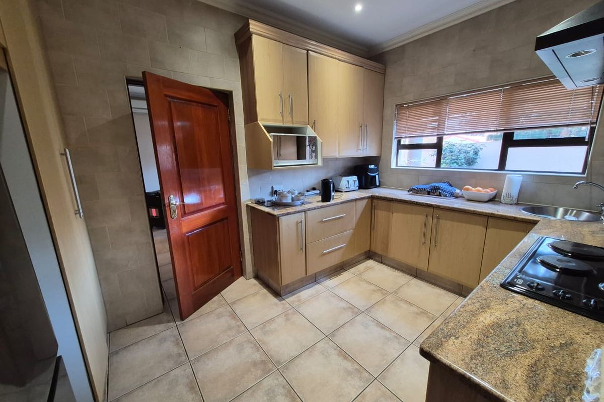 A functional kitchen featuring light wood cabinetry, granite countertops, ceramic tile flooring, and a built-in hob with an extractor fan.