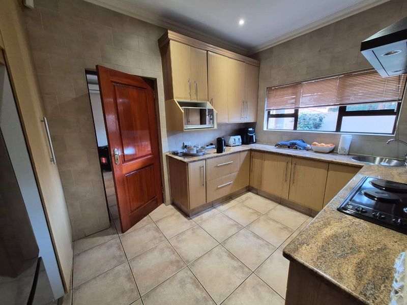 A functional kitchen featuring light wood cabinetry, granite countertops, ceramic tile flooring, and a built-in hob with an extractor fan.